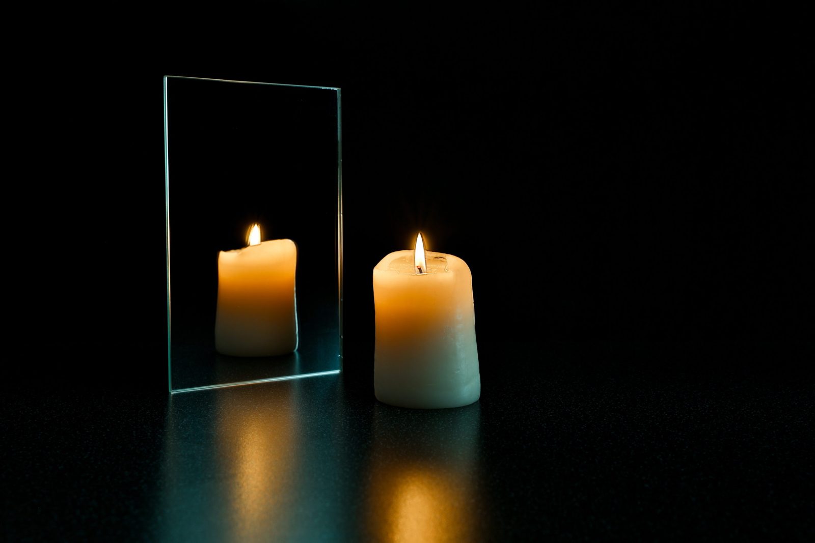burning candle and mirror on a black background. reflection of a candle flame in a mirror in the dark