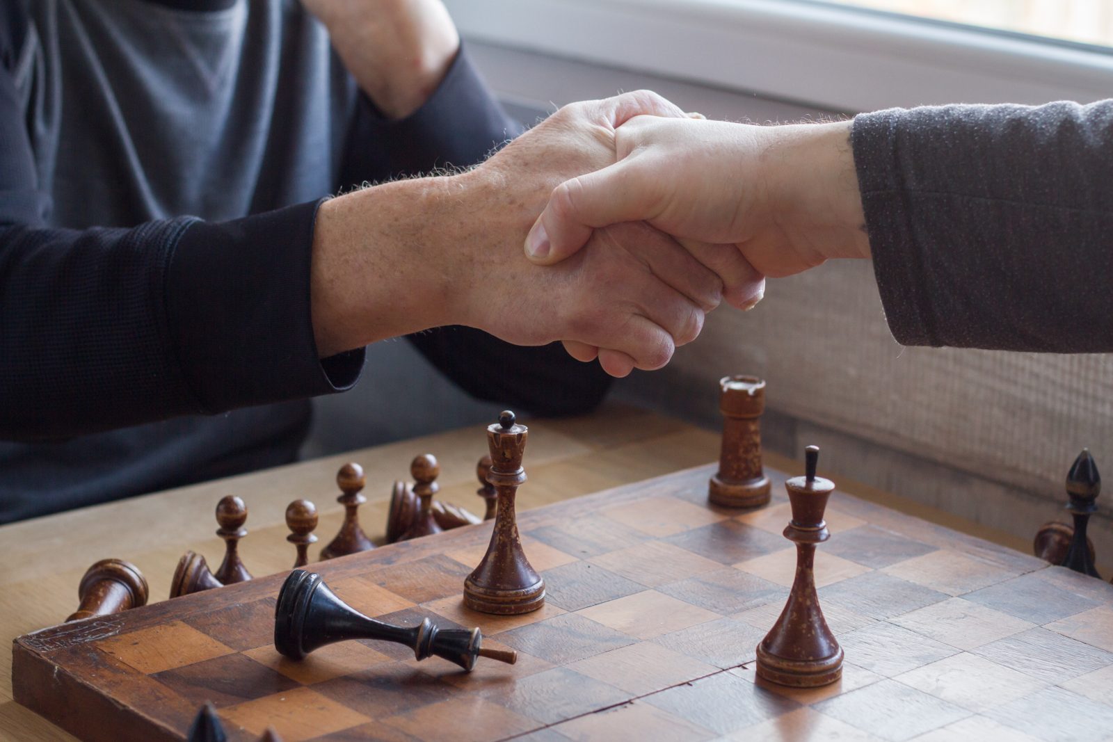 An old man shakes hands with an opponent in a game of chess, he lost and acknowledges it.