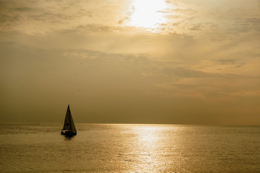 Sunset in the sea, a small sailing boat at sunset away