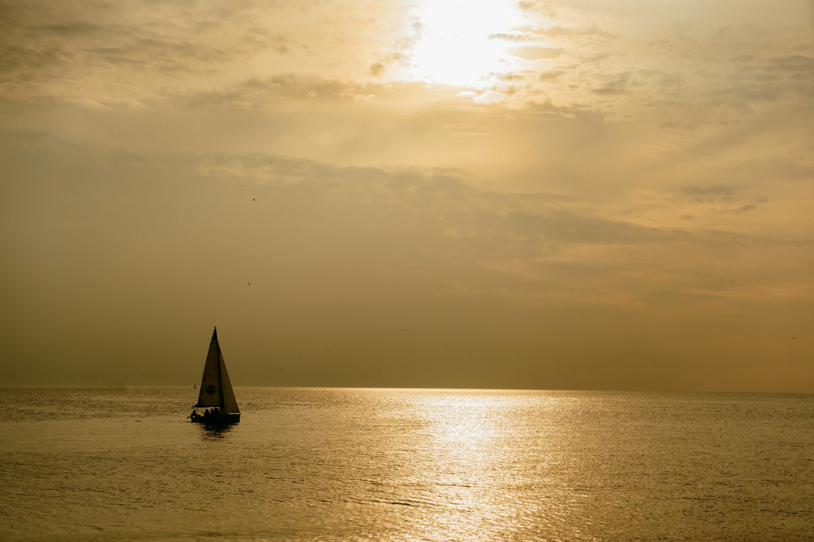 Sunset in the sea, a small sailing boat at sunset away