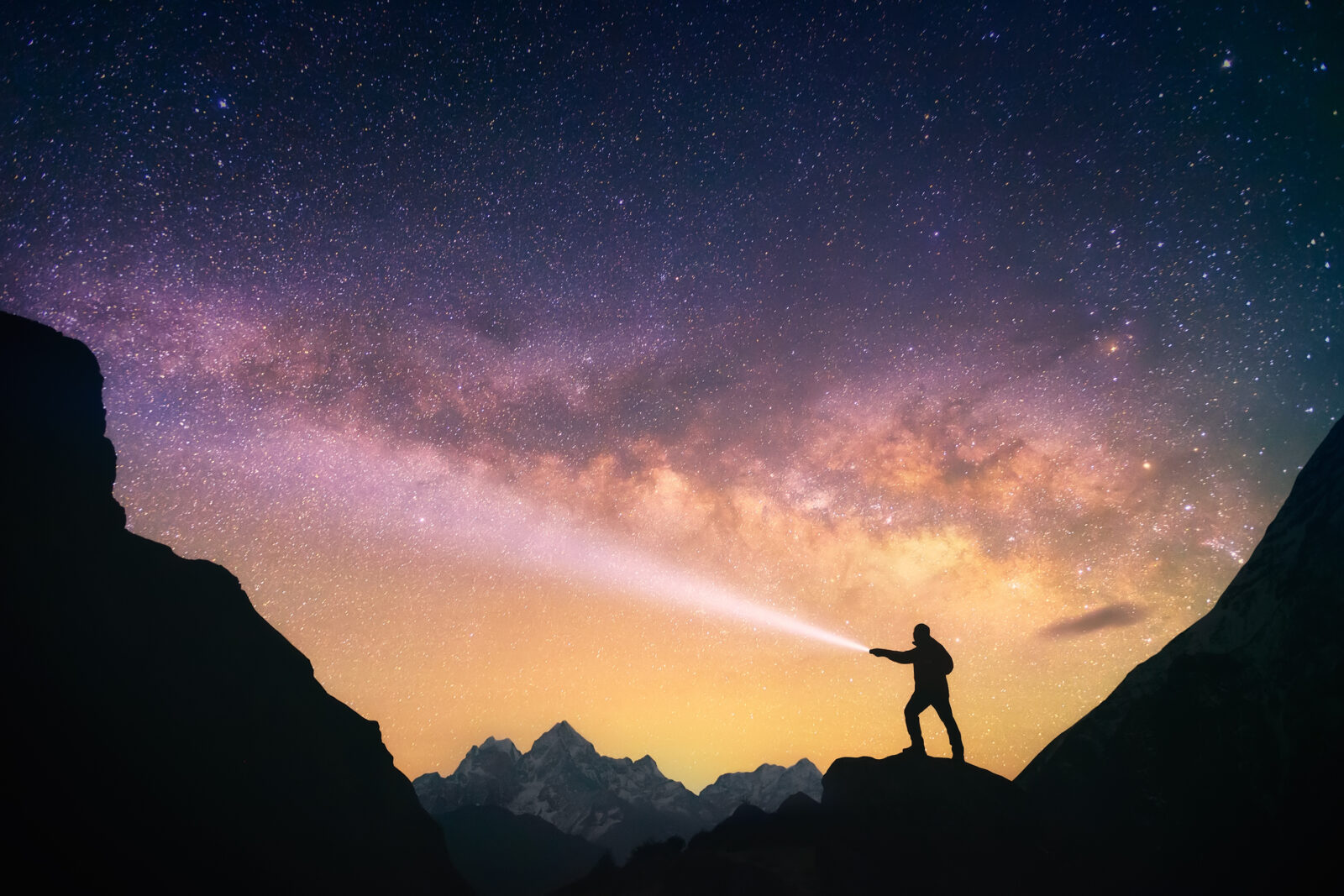Silhouette of the man standing against the Milky Way in the mountains with a flashlight in his hands. Nepal, Everest region, view of the mount Thamserku (6,608 m) from Thame village (3,750 m).