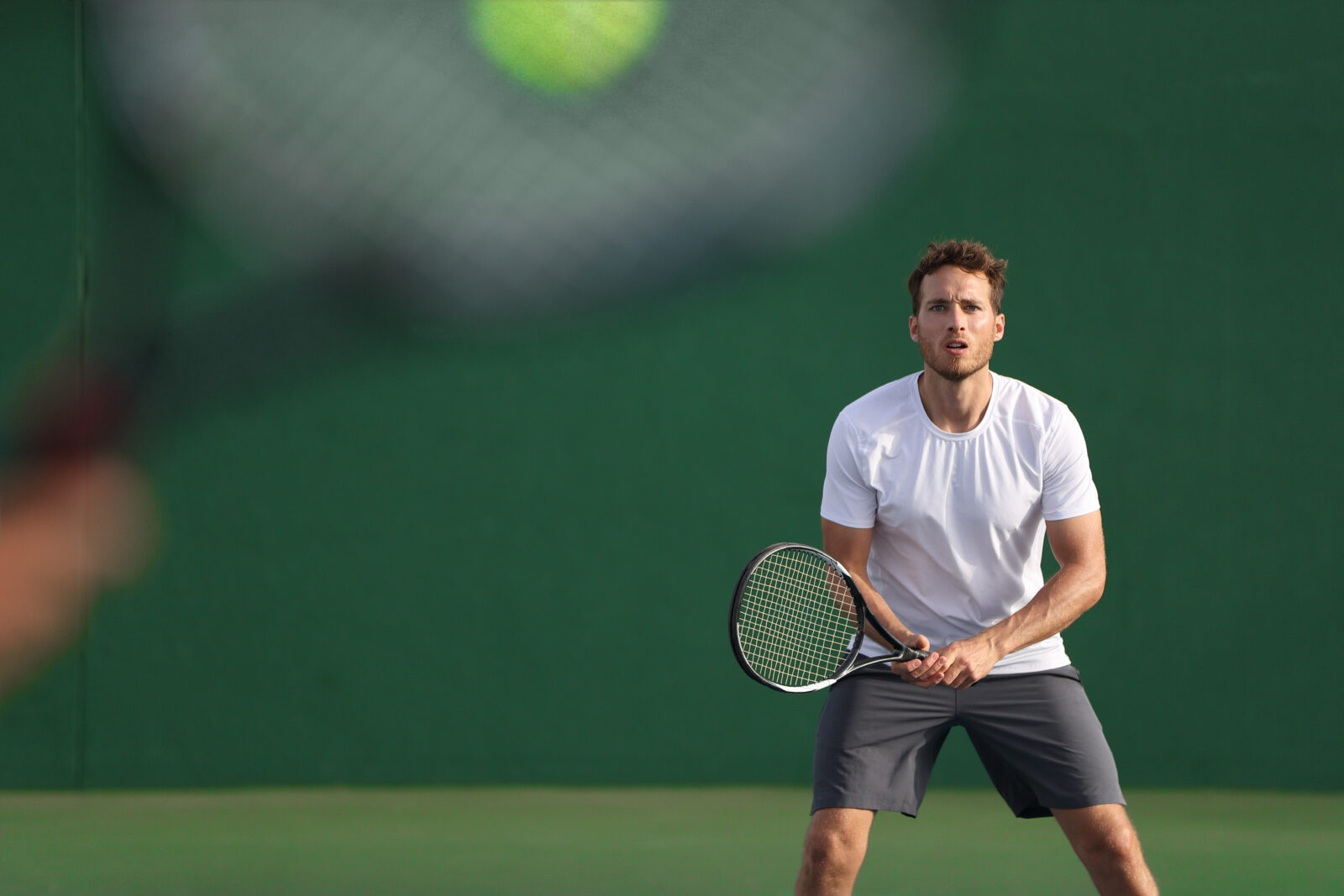 Tennis player focused on other player hitting ball with racket on court. Men sport athletes players playing tennis match together. Two professional tennis players on hard outdoor court during game.