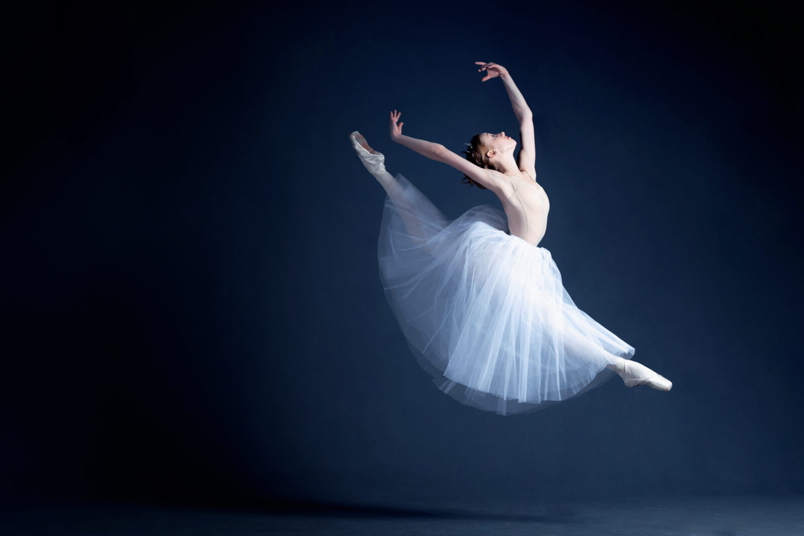 Young ballerina in a beautiful dress is dancing in a dark photostudio