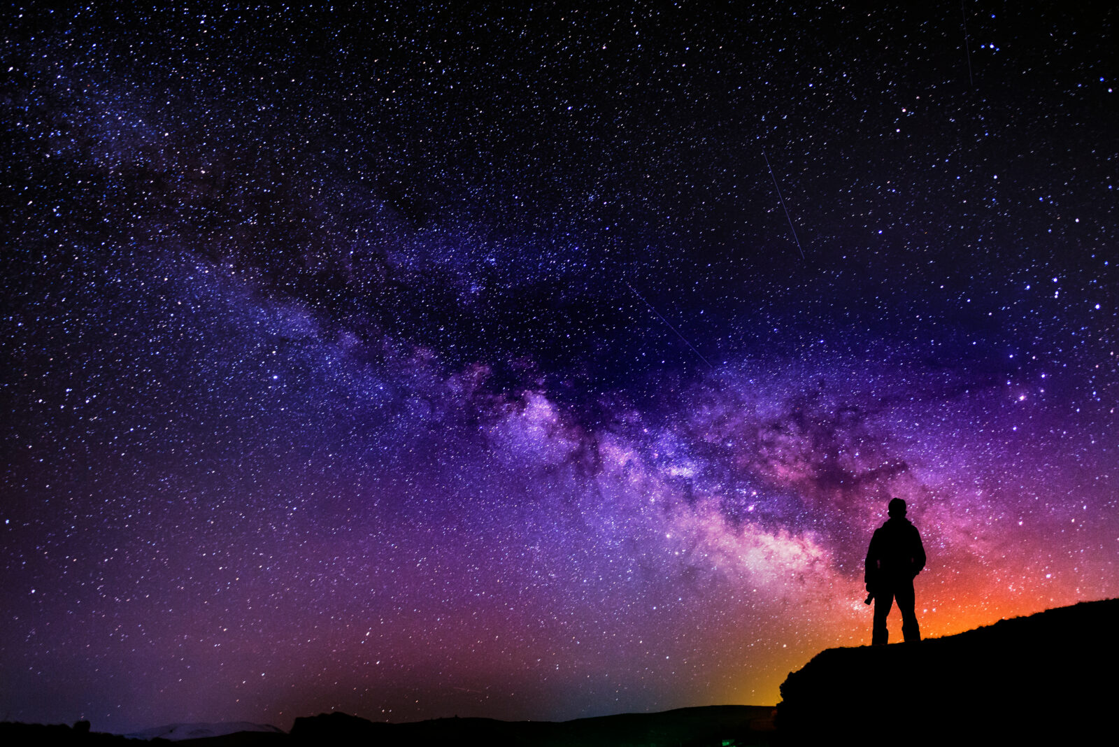 Beautiful starry night, man silhouette with a camera looking at the Milky Way galaxy.